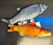 Load image into Gallery viewer, Two fish-shaped toys, one orange and yellow, the other gray and white, on a dark surface.